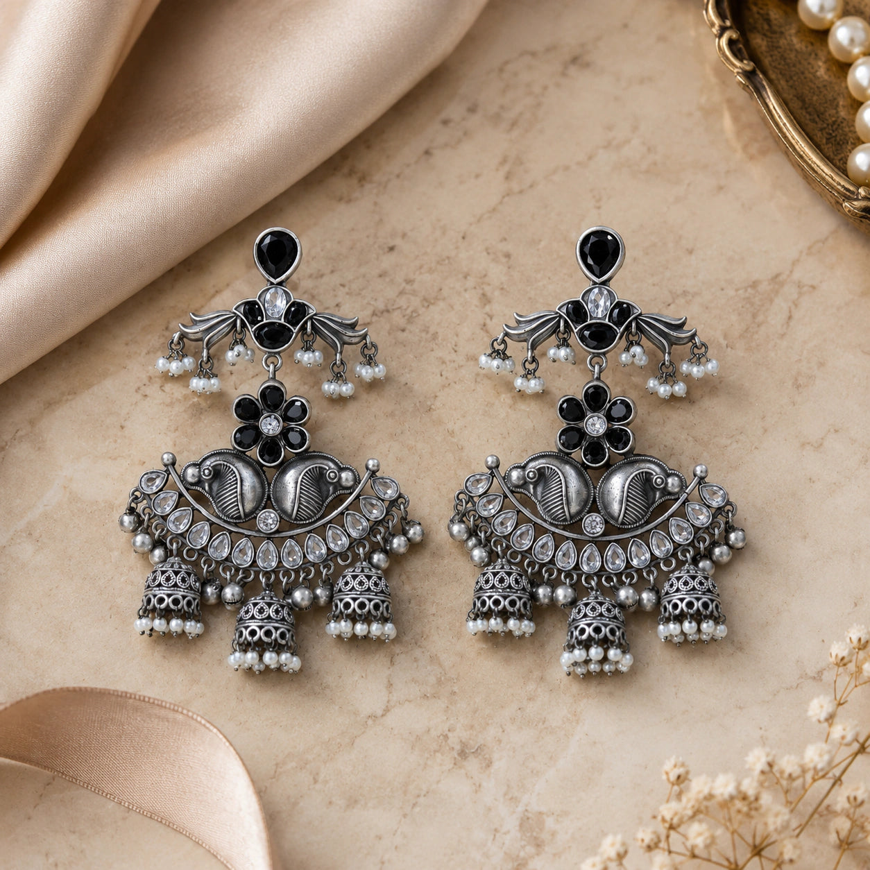 Black pearl-style chandelier earrings styled in an elegant jewellery flat lay