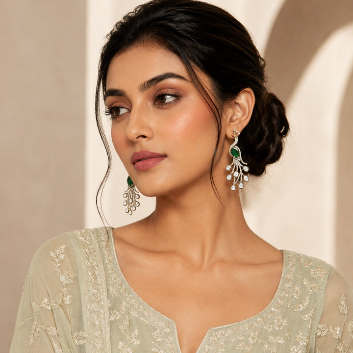 Antique gold green peacock earrings on a dark jewellery studio display