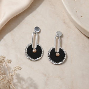 Close-up of black geometric forms, silver accents and pearl-style drops