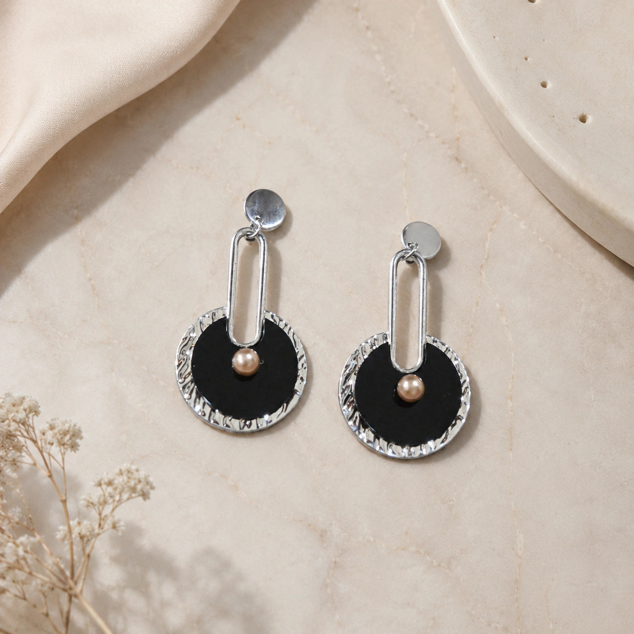 Close-up of black geometric forms, silver accents and pearl-style drops