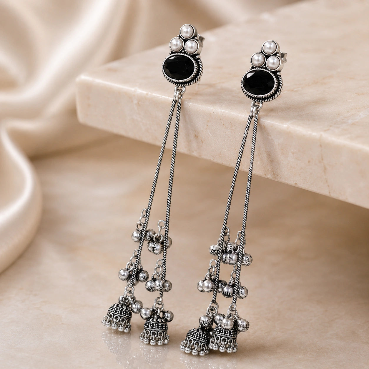 Black pearl-style jhumka earrings styled in an elegant jewellery flat lay