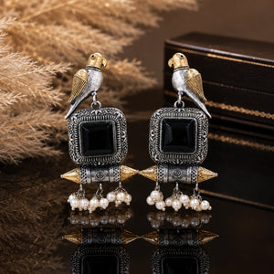 Black-stone bird pearl-style earrings on a dark jewellery studio display