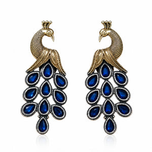 Angled view of German silver peacock earrings with blue-stone chandelier drops