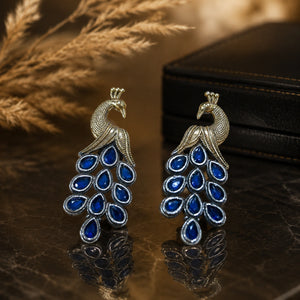 Blue-stone peacock chandelier earrings on a glossy dark reflective jewellery display