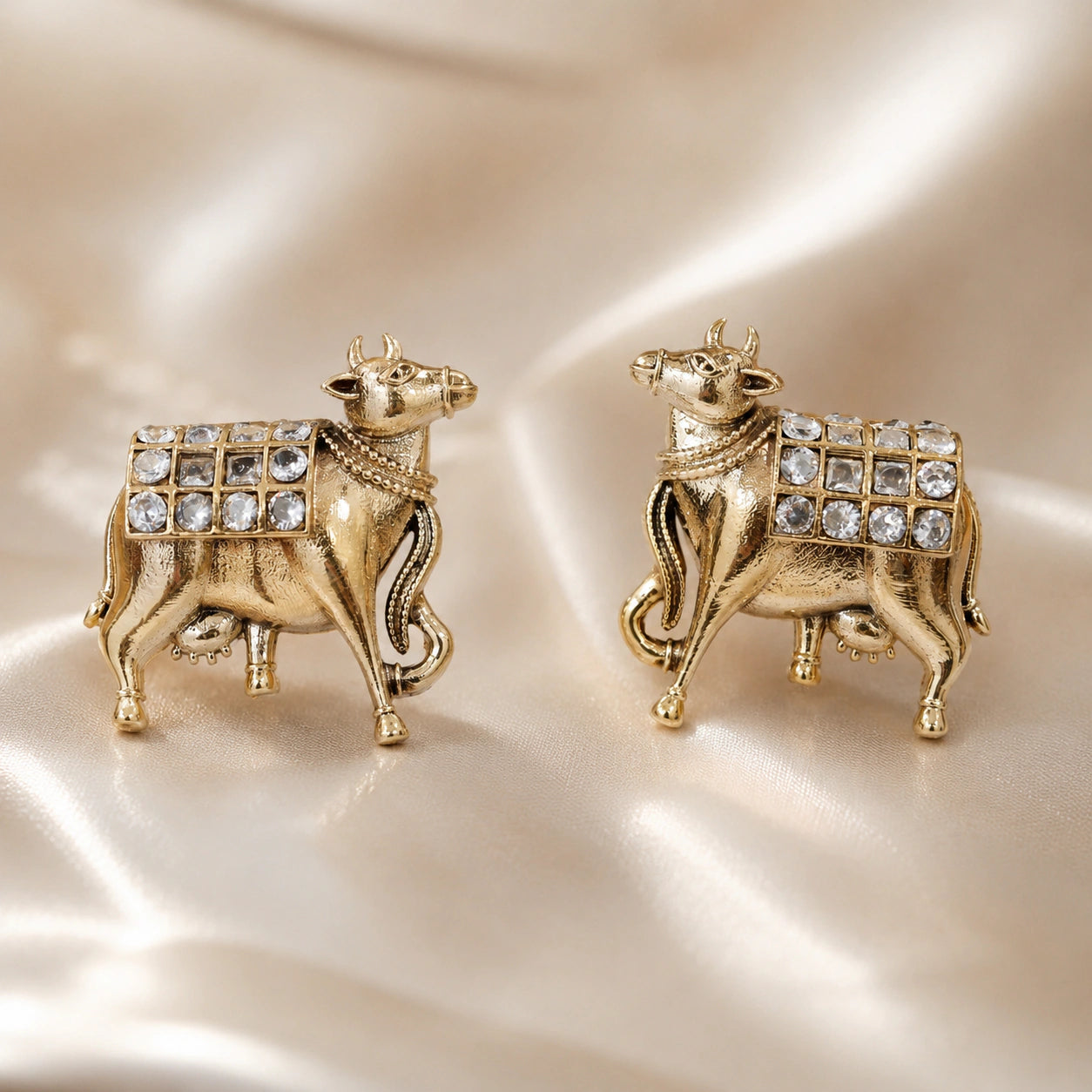 Gold cow-motif crystal drop earrings on a dark jewellery studio display