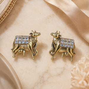 Gold cow-motif crystal drop earrings styled in an elegant jewellery flat lay