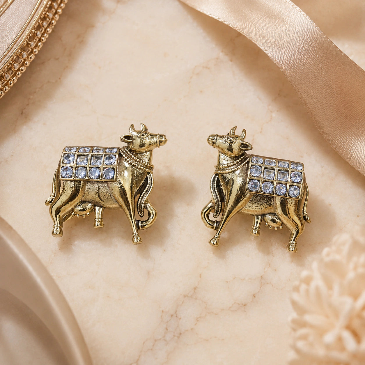 Gold cow-motif crystal drop earrings styled in an elegant jewellery flat lay