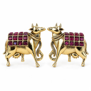 Gold maroon cow-motif dangle earrings on a dark jewellery studio display