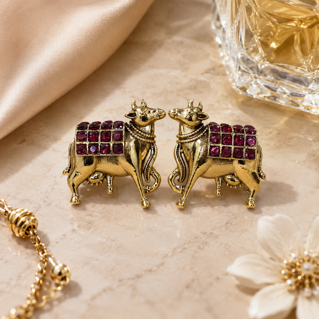 Gold maroon cow-motif dangle earrings styled in an elegant jewellery flat lay