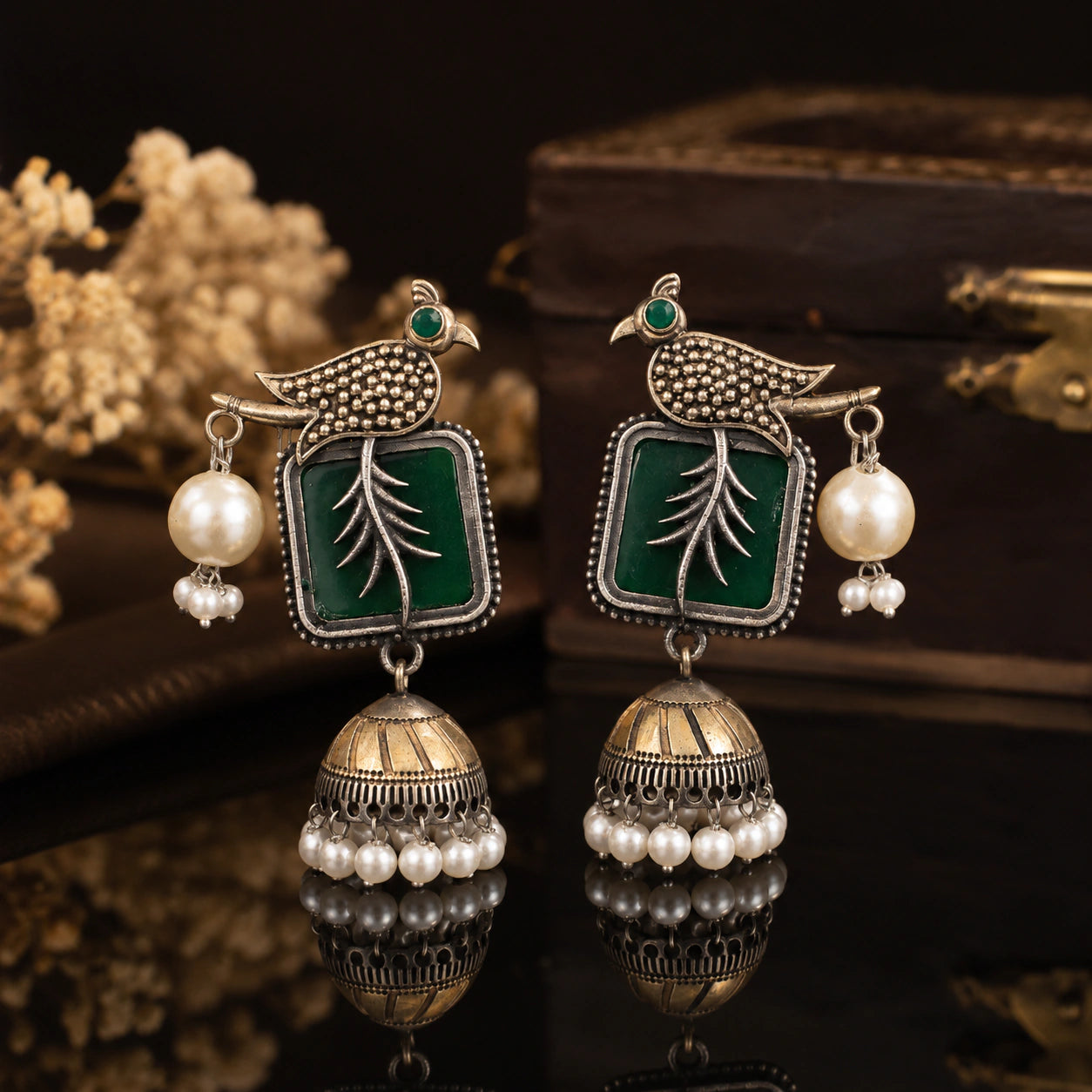 Green bird-motif pearl jhumka earrings on a dark jewellery studio display