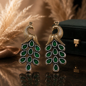 Green peacock chandelier earrings on a glossy dark reflective jewellery display