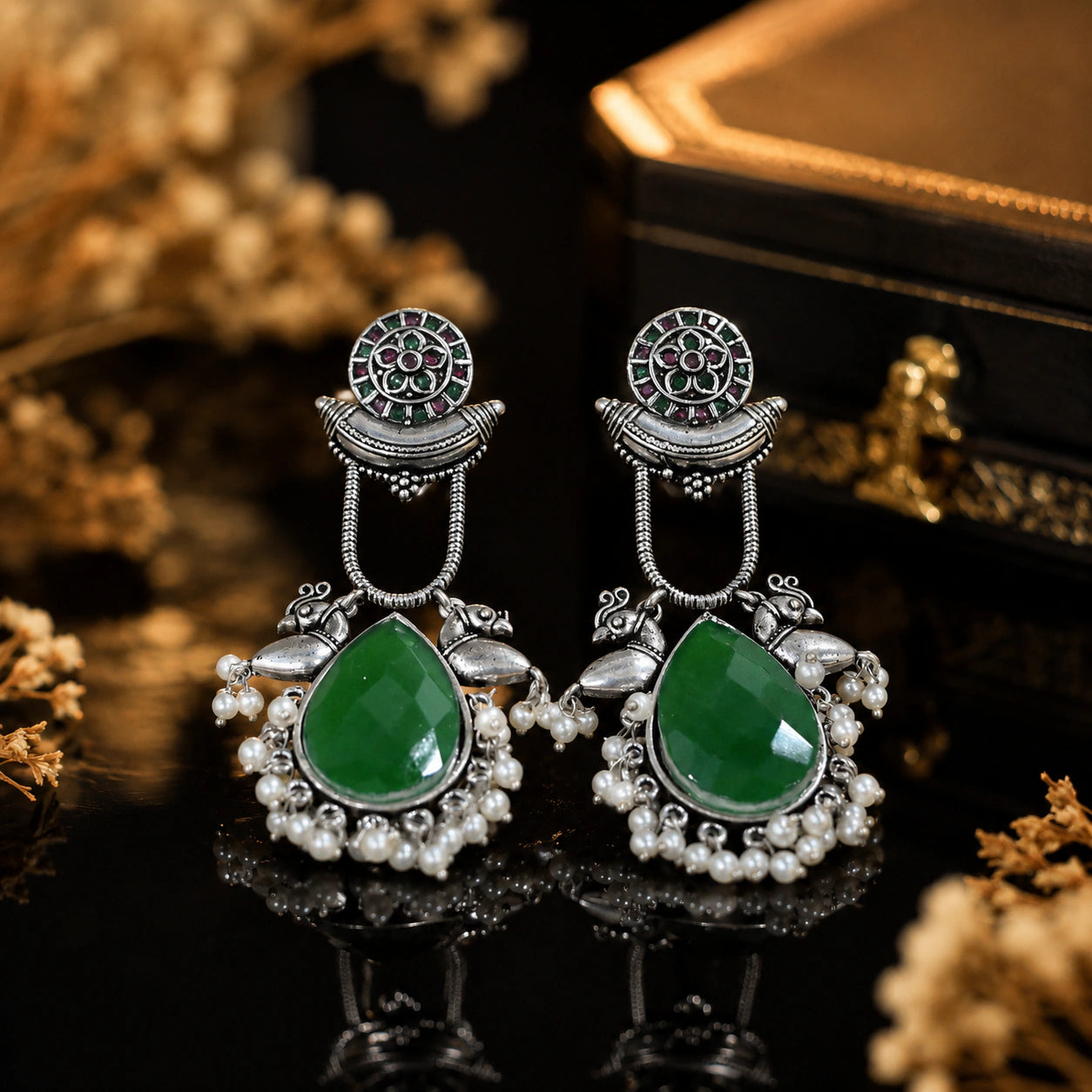Green pearl bird-motif earrings on a dark jewellery studio display