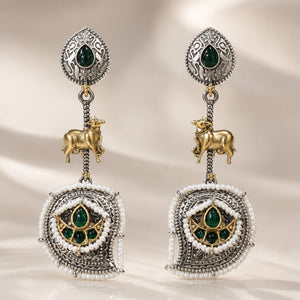 Green pearl cow-motif earrings on a dark jewellery studio display