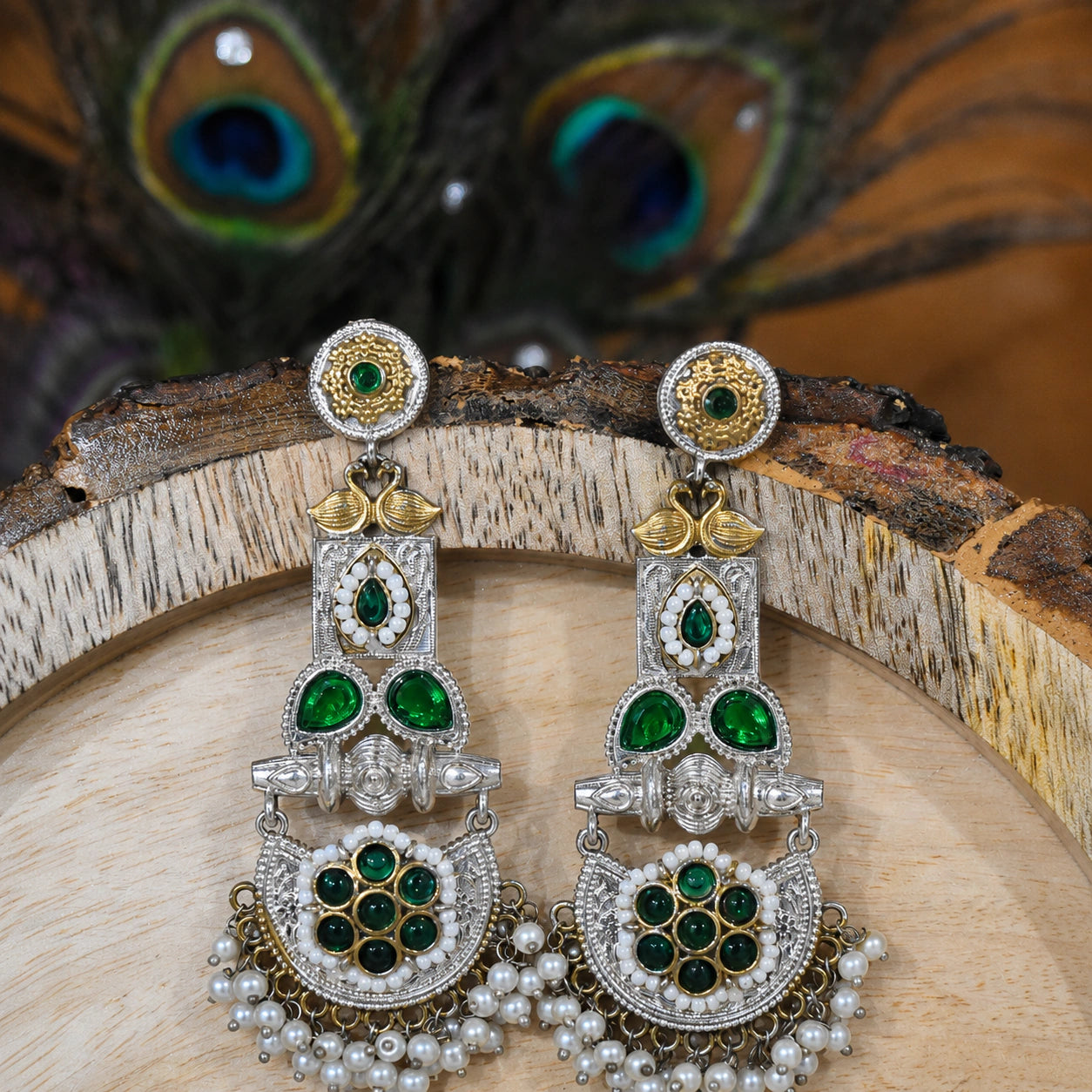 Green pearl peacock chandelier earrings on a dark jewellery studio display