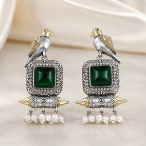 Green-stone bird pearl dangle earrings on a dark jewellery studio display