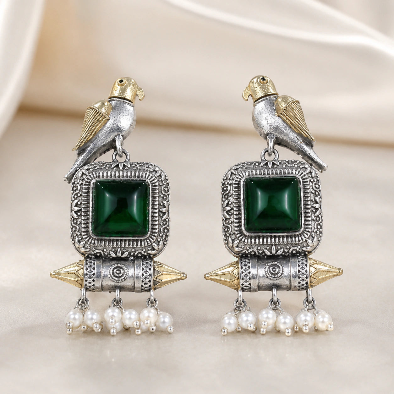 Green-stone bird pearl dangle earrings on a dark jewellery studio display