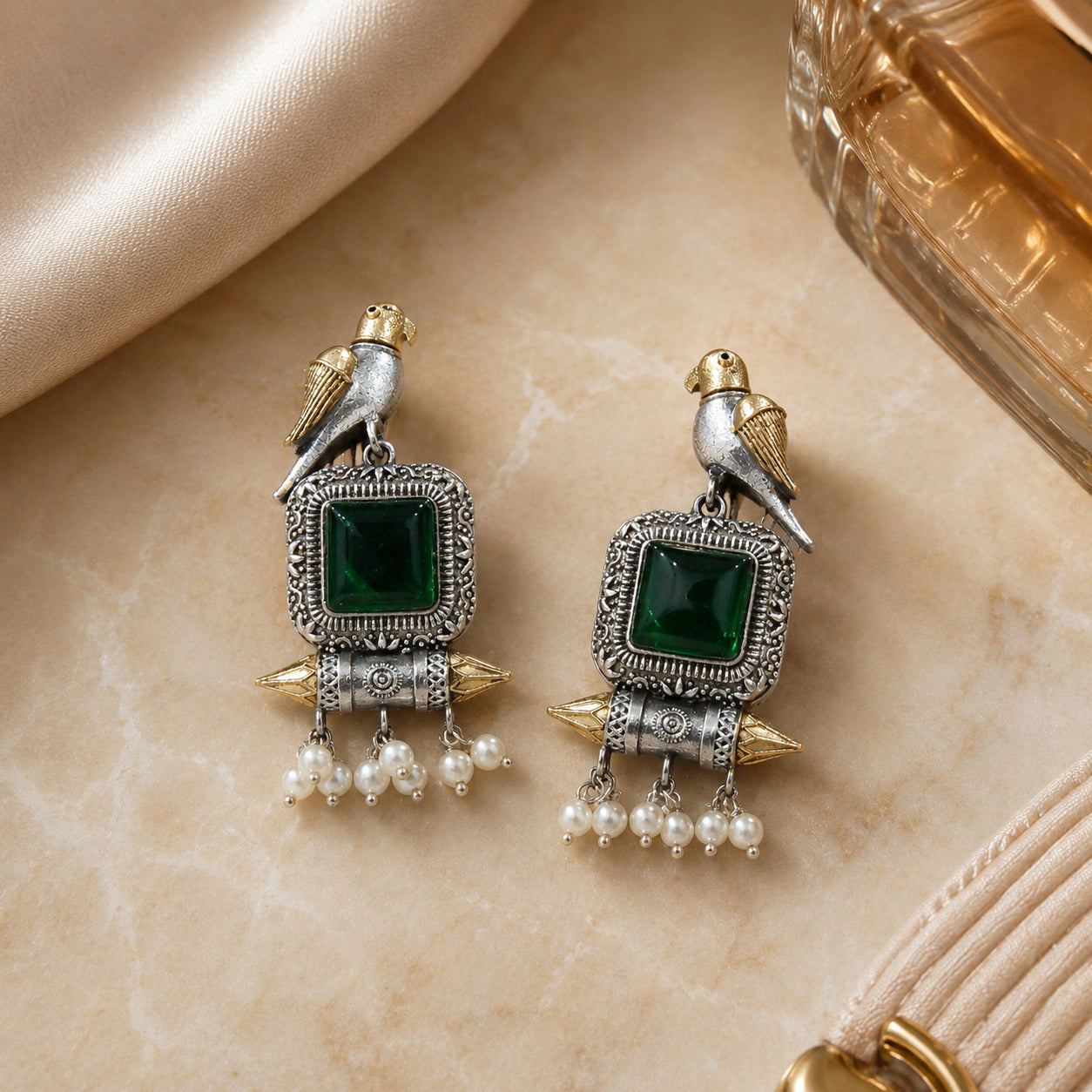 Green-stone bird pearl dangle earrings styled in an elegant jewellery flat lay