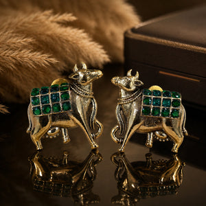 Green-stone cow-motif earrings on a dark jewellery studio display