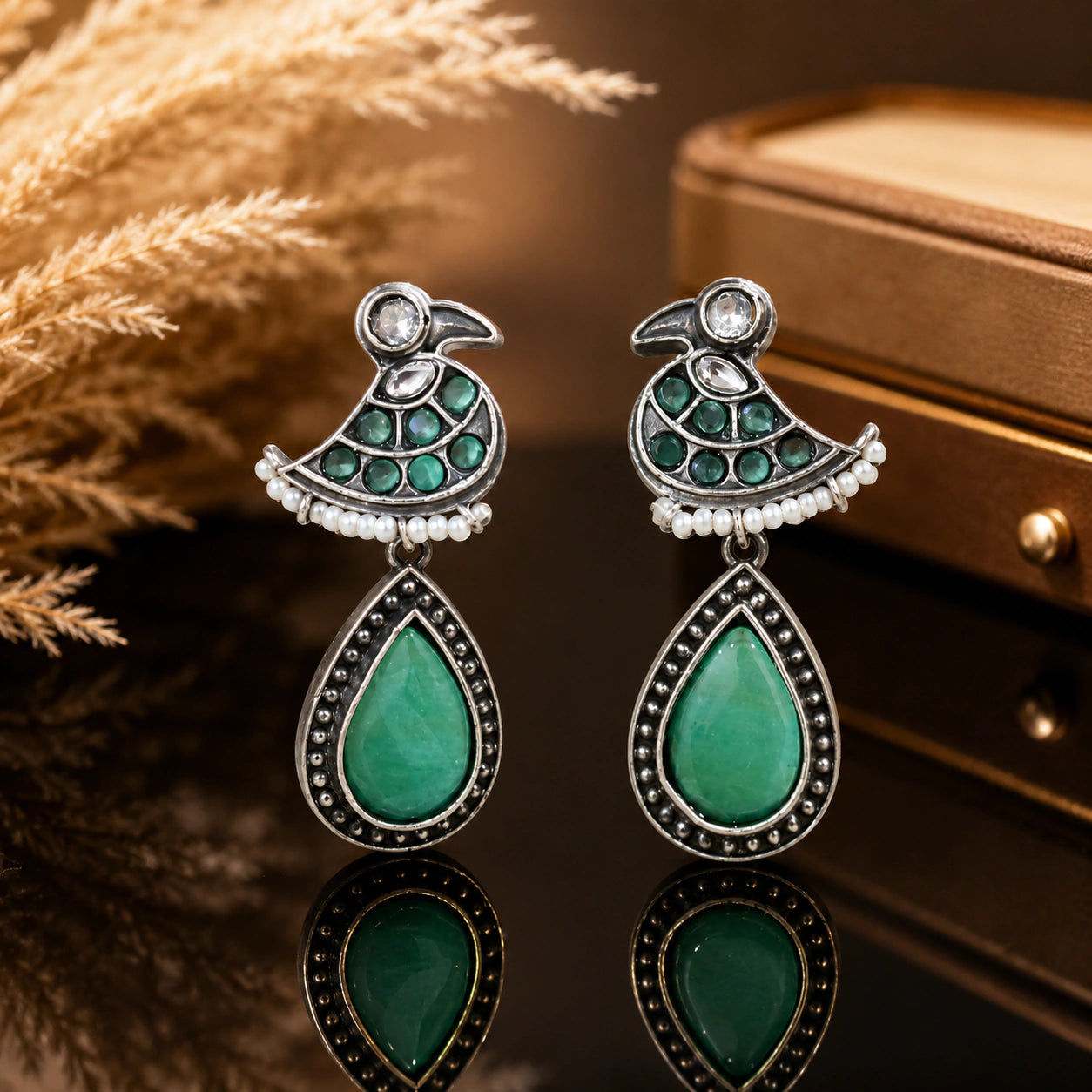 Green-stone pearl-style dangle earrings on a dark jewellery studio display