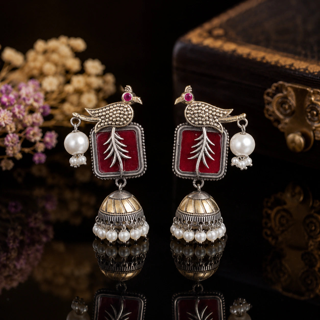 Maroon bird pearl jhumka earrings on a dark jewellery studio display