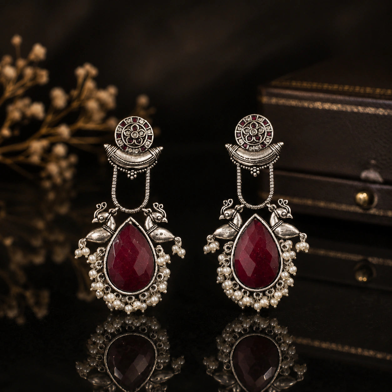 Maroon pearl bird-motif earrings on a dark jewellery studio display