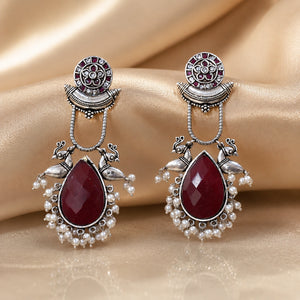 Maroon pearl bird-motif earrings styled in an elegant jewellery flat lay