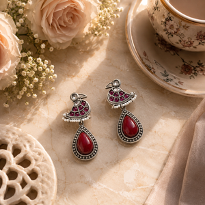 Maroon pearl bird dangle earrings styled in an elegant jewellery flat lay