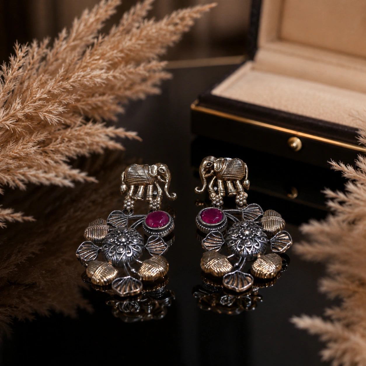 Maroon-stone chandelier earrings on a dark jewellery studio display