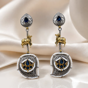 Navy pearl cow-motif chandelier earrings on a dark jewellery studio display
