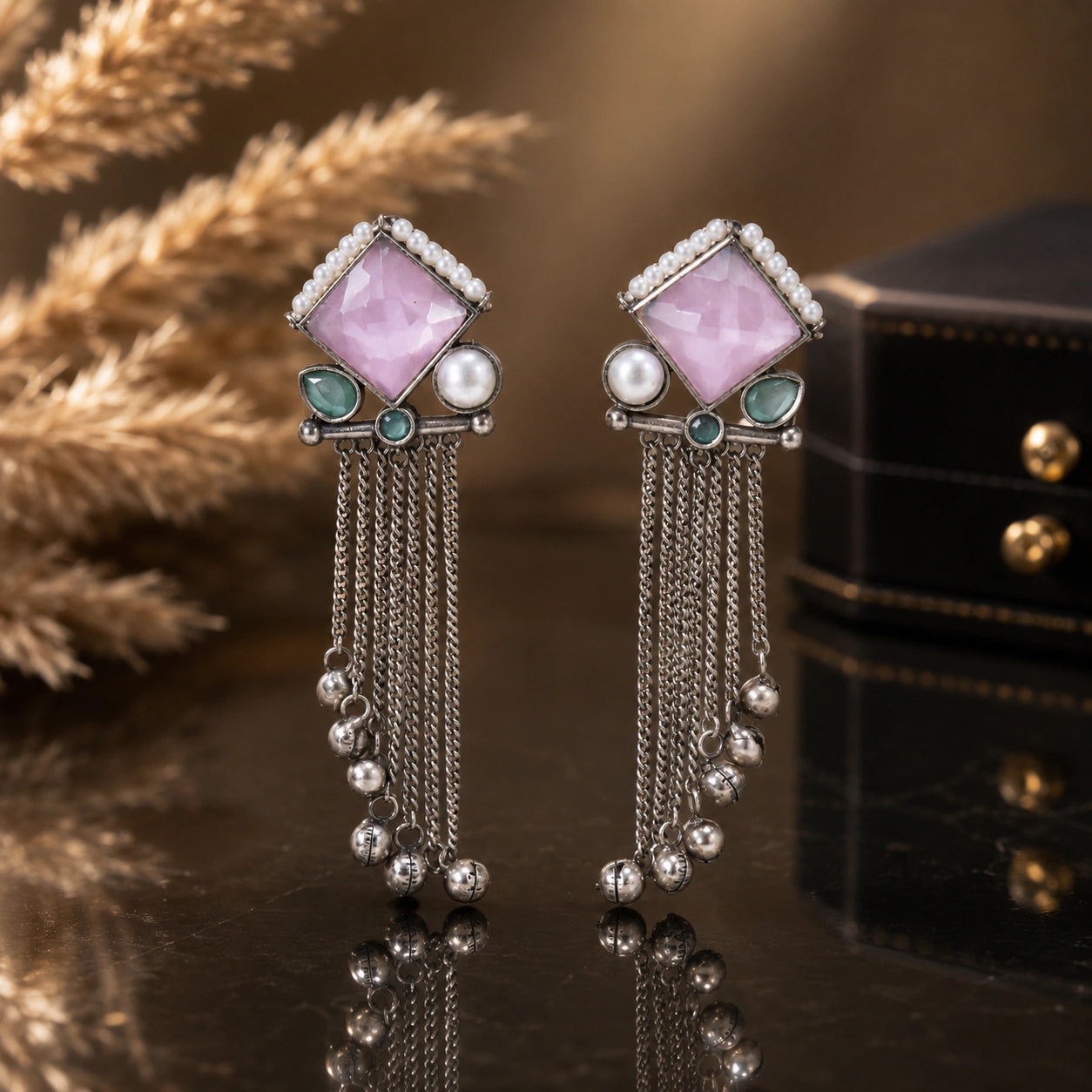 Pink pearl-style dangle earrings on a glossy dark reflective jewellery display