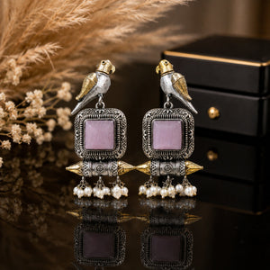 Pink-stone bird pearl dangle earrings on a dark jewellery studio display
