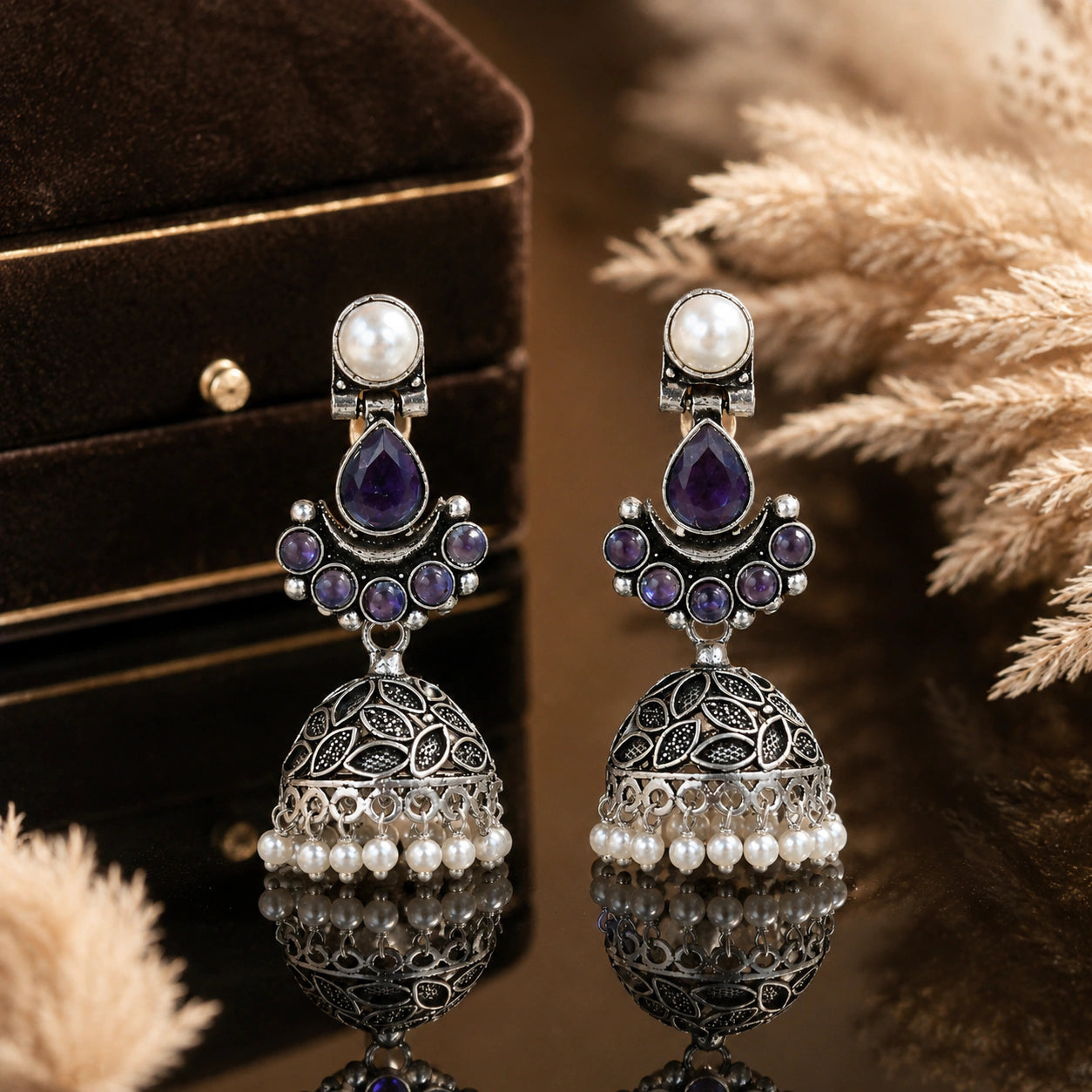 Purple pearl leaf dome jhumka earrings on a glossy dark reflective display