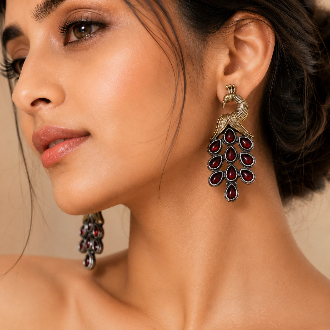 Angled view of German silver peacock earrings with red chandelier drops