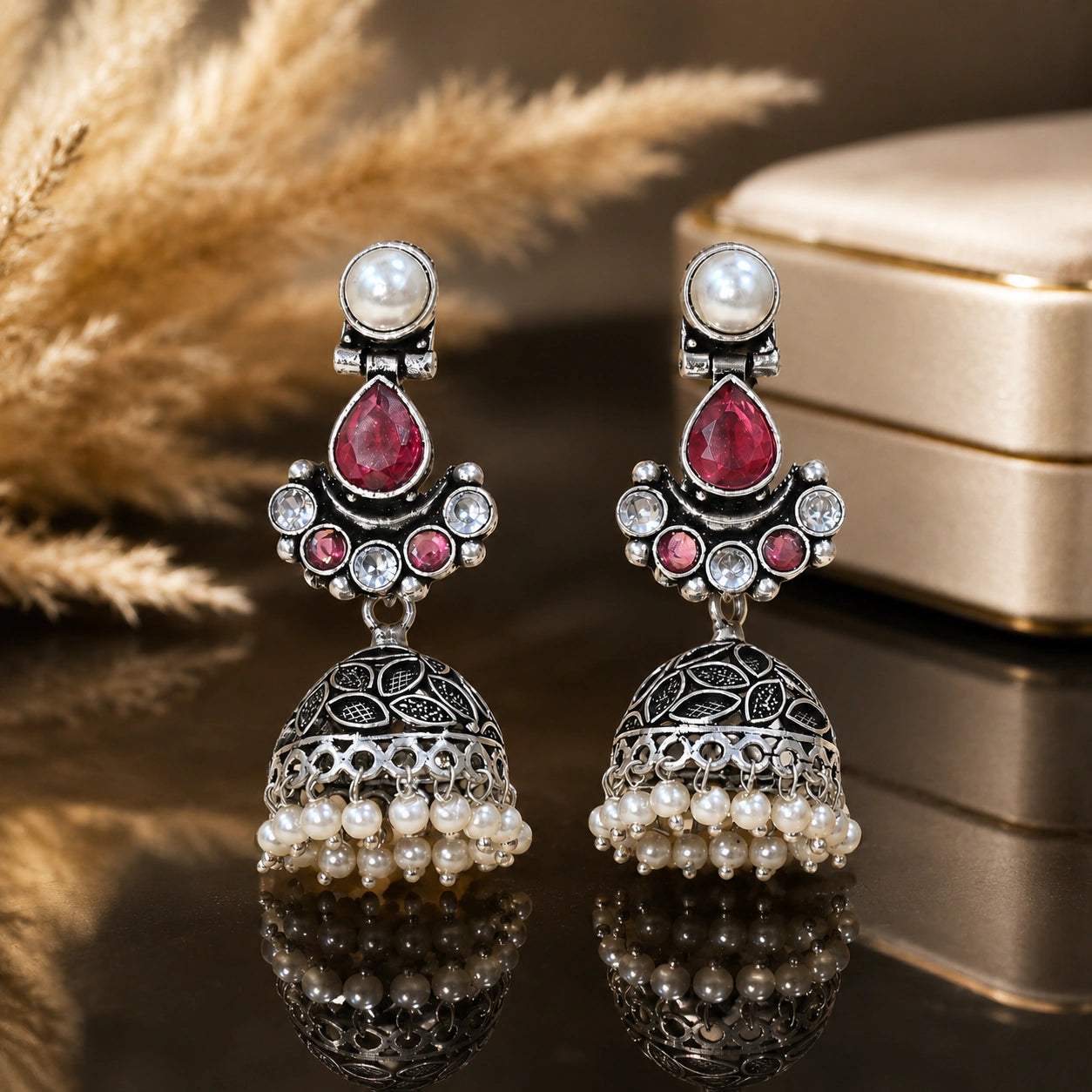 Ruby-tone pearl leaf jhumka earrings on a glossy dark reflective display