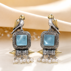 Angled view of German silver sky blue bird pearl-style dangle earrings