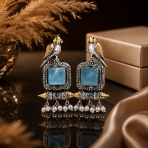 Sky blue bird pearl-style earrings on a dark jewellery studio display
