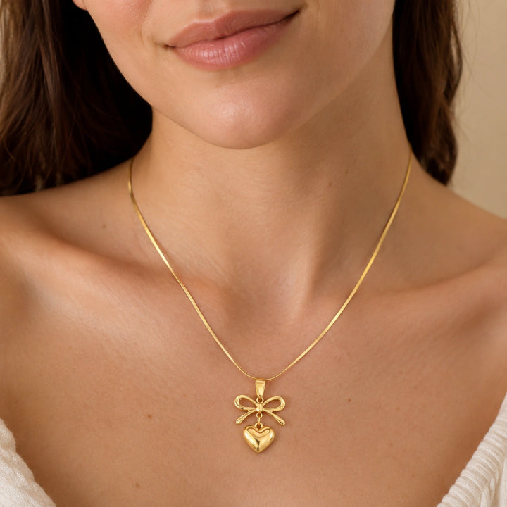 Gold bow heart pendant necklace on a dark jewellery studio display