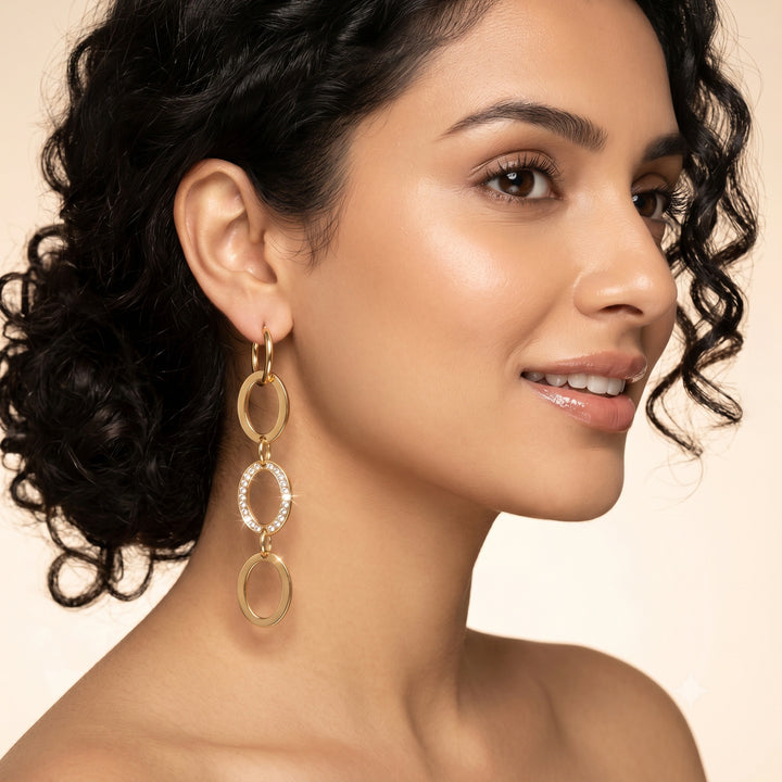 Gold crystal oval-link earrings on a dark jewellery studio display