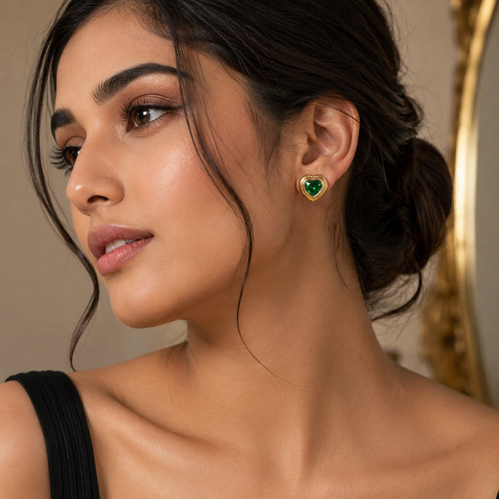 Gold emerald heart crystal studs on a dark jewellery studio display