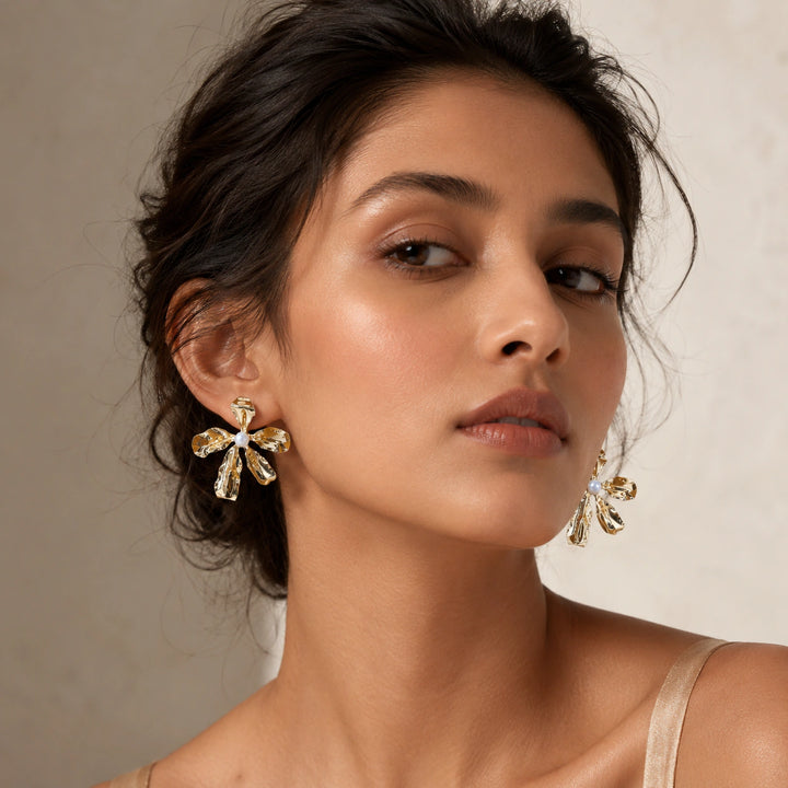 Gold floral pearl statement earrings on a dark jewellery studio display