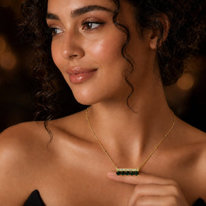 Gold green stone crystal-bar necklace on a dark jewellery studio display