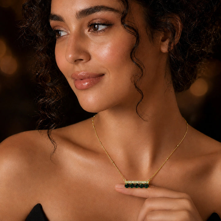 Gold green stone crystal-bar necklace on a dark jewellery studio display