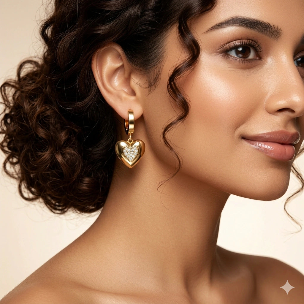 Angled view of gold heart charm huggie hoop earrings