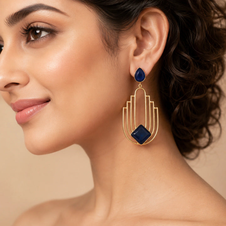 Gold navy geometric chandelier earrings on a dark jewellery studio display