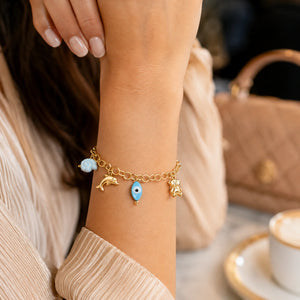 Gold ocean charm bracelet styled in a beach-inspired jewellery flat lay