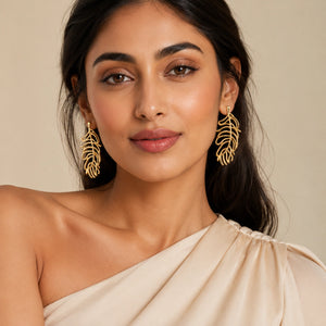 Gold tropical leaf earrings on a dark jewellery studio display