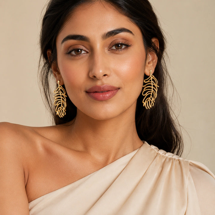 Gold tropical leaf earrings on a dark jewellery studio display