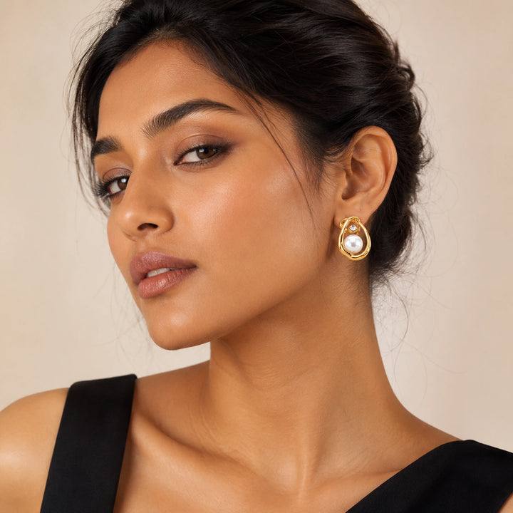 Gold organic teardrop pearl studs on a dark jewellery studio display