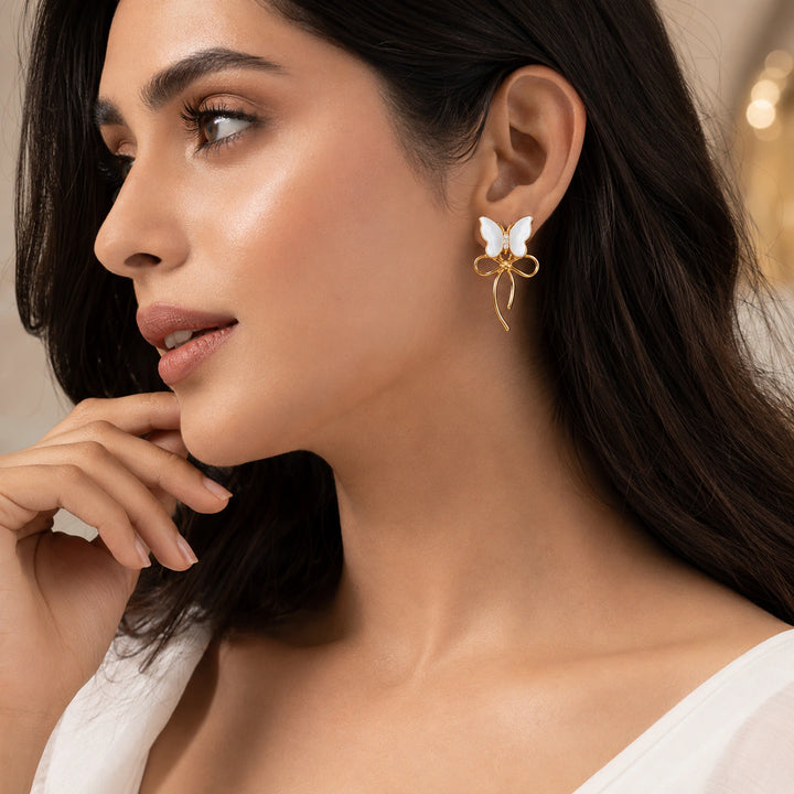 Gold pearl butterfly bow earrings on a dark jewellery studio display
