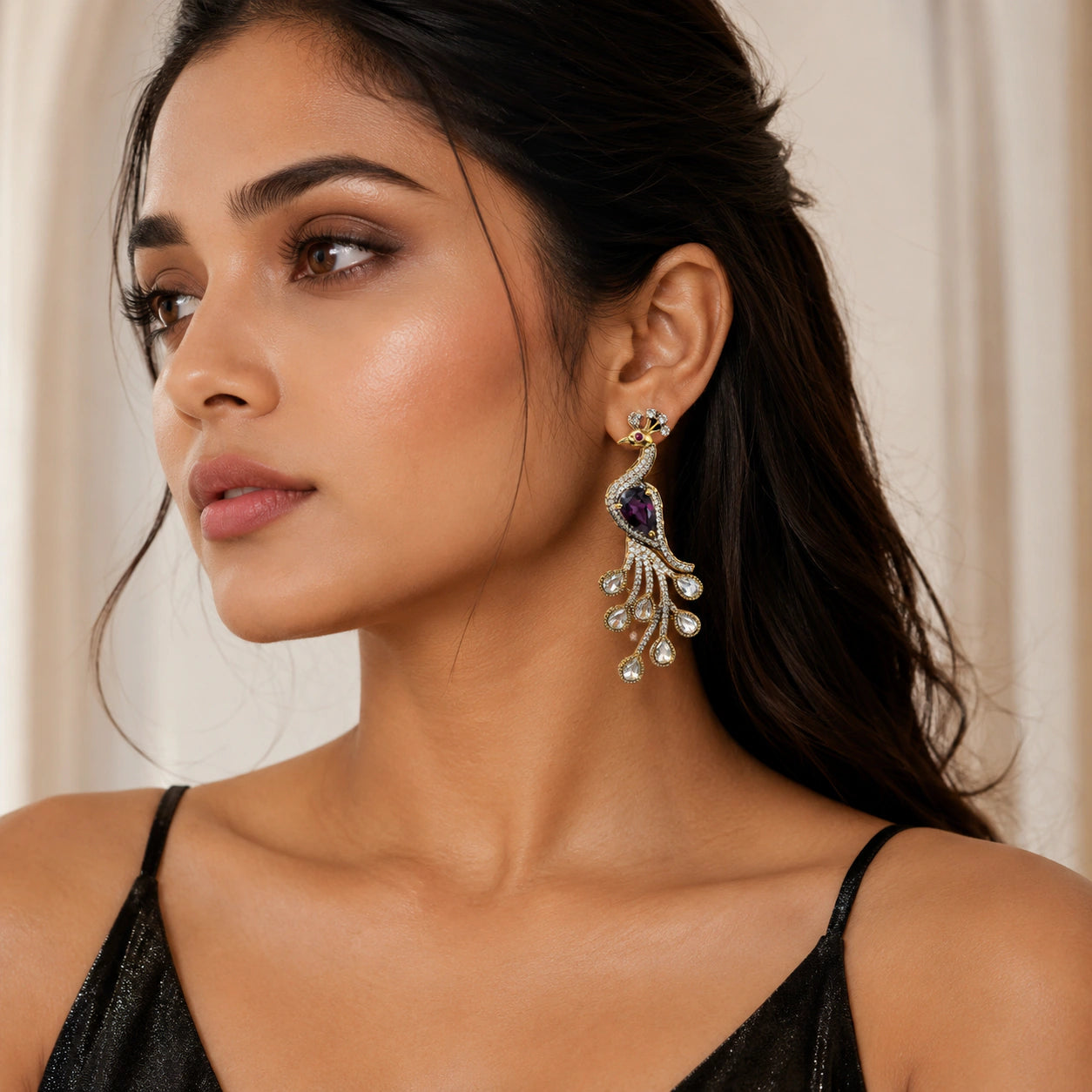 Gold-tone purple peacock earrings on a dark jewellery studio display